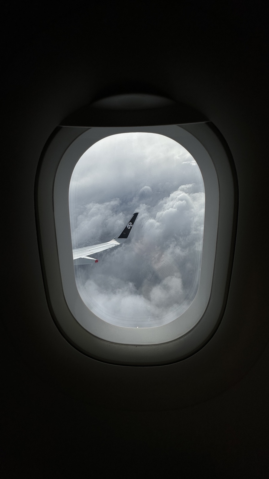An airplane wingtip over cloud towers, framed by the cabin window